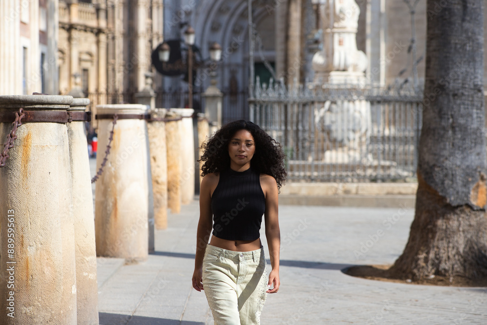 beautiful young latin woman with dark eyes and long curly hair walks through the centre of Seville, in the background you can see the cathedral of catholic worship and gothic style of Seville, Spain. beautiful young latin woman with dark eyes and long curly hair walks through the centre of Seville, in the background you can see the cathedral of catholic worship and gothic style of Seville, Spain.