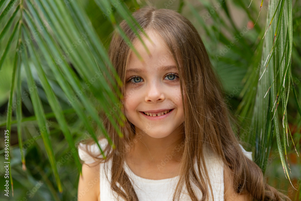 The face of a little girl surrounded by tropical leaves. Closeup portrait of a beautiful child with perfect skin and dark hair. Natural cosmetics, health, cleanliness, skin care, beauty concept The face of a little girl surrounded by tropical leaves. Closeup portrait of a beautiful child with perfect skin and dark hair. Natural cosmetics, health, cleanliness, skin care, beauty concept