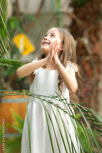 Little girl in the botanical garden. a girl in a white dress laughs near palm leaves.