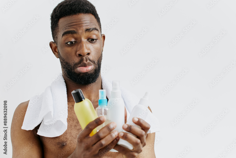 Confident shirtless black man displaying skincare routine with lotion and shampoo bottles in hands Confident shirtless black man displaying skincare routine with lotion and shampoo bottles in hands