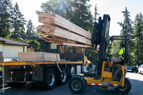 Foto Forklift unloading a load of lumber from a flatbed delivery truck in a residenti