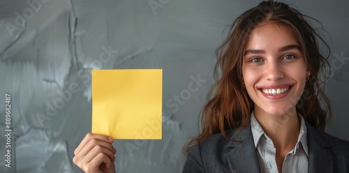 Smiling Woman Holding Blank Yellow Card in Front of Gray Wall