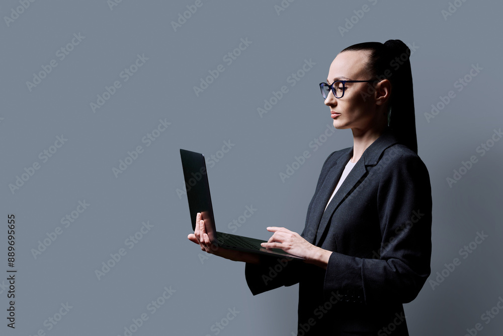 Middle-aged business confident woman using laptop on gray background Middle-aged business confident woman using laptop on gray background