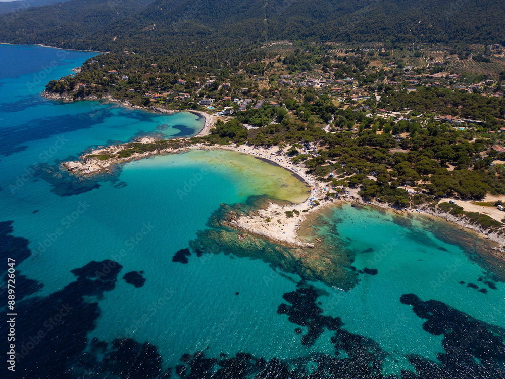 Aerial view of an island on Sithonia Peninsula, Greece, with beaches and rocks, surrounded by crystal-clear waters. Yachts and boats anchor in turquoise waters. Nearby islets and reefs visible Aerial view of an island on Sithonia Peninsula, Greece, with beaches and rocks, surrounded by crystal-clear waters. Yachts and boats anchor in turquoise waters. Nearby islets and reefs visible