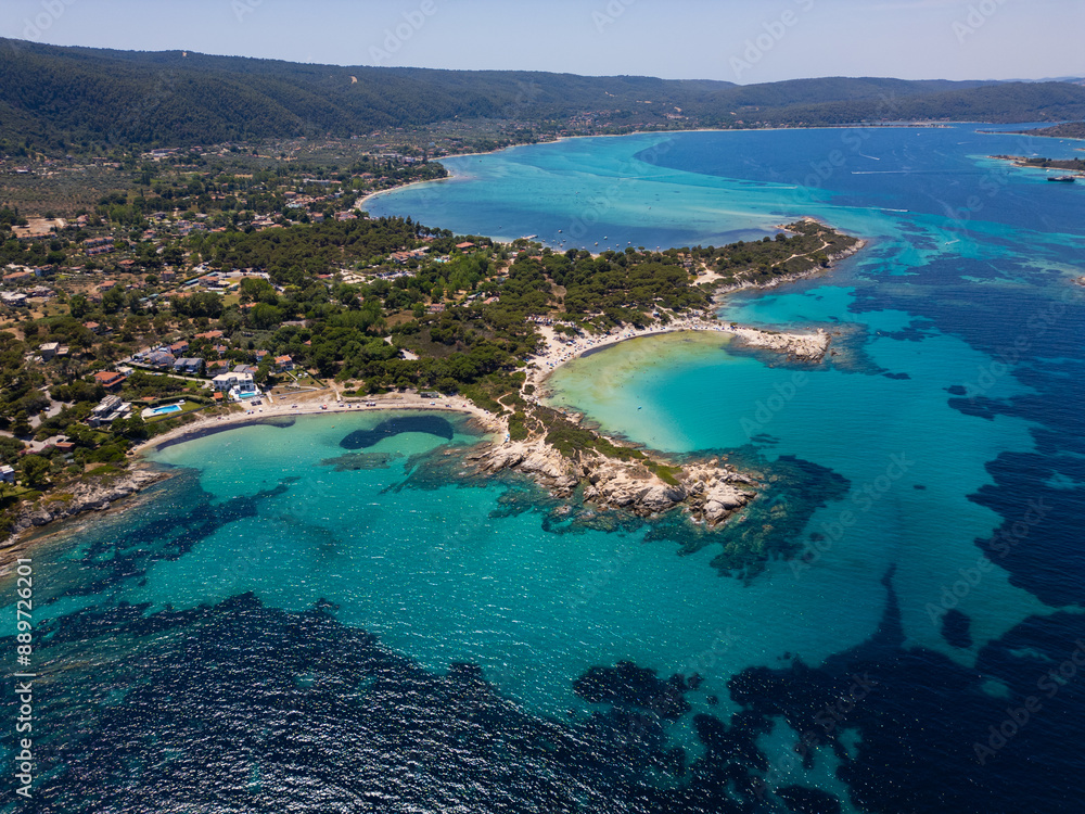 Aerial view of an island on Sithonia Peninsula, Greece, with beaches and rocks, surrounded by crystal-clear waters. Yachts and boats anchor in turquoise waters. Nearby islets and reefs visible Aerial view of an island on Sithonia Peninsula, Greece, with beaches and rocks, surrounded by crystal-clear waters. Yachts and boats anchor in turquoise waters. Nearby islets and reefs visible