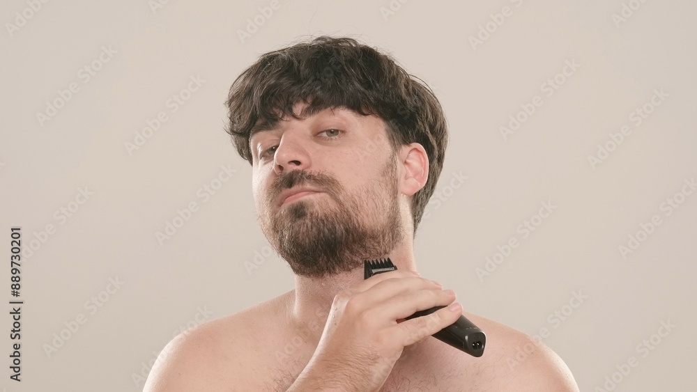 Obraz premium Young adult man shaving trimming beard with shaving machine, isolated on white background. Natural beauty skin care concept.