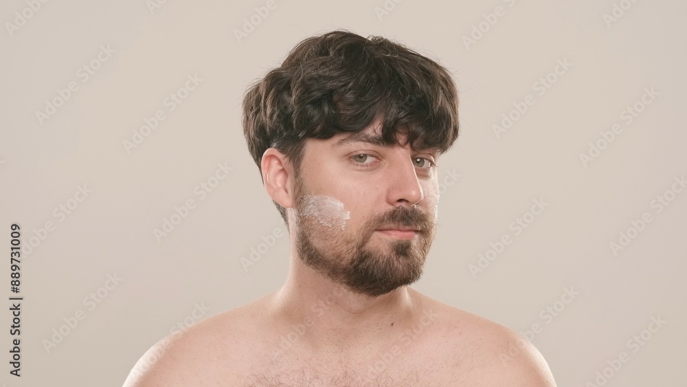 Young adult man applies aftershave cream moisturizer looks at camera, isolated on white background. Natural beauty skin care concept Young adult man applies aftershave cream moisturizer looks at camera, isolated on white background. Natural beauty skin care concept