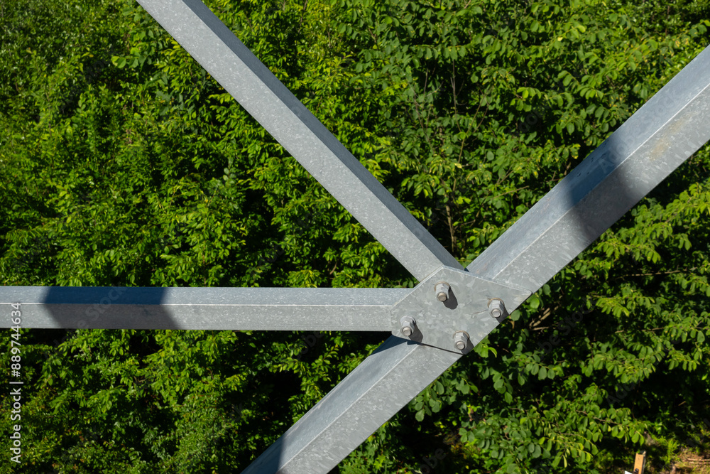 Bolted connections of steel elements of the observation tower. Construction details of galvanized steel against a green trees background