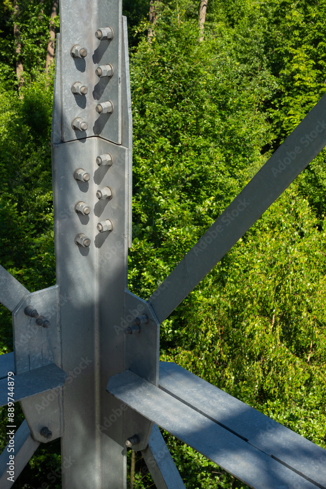 Bolted connections of steel elements of the observation tower. Construction details of galvanized steel against a green trees background