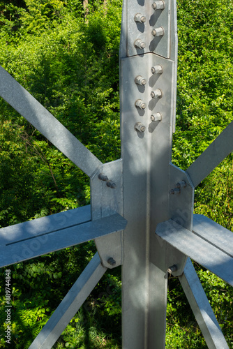 Obraz na płótnie Bolted connections of steel elements of the observation tower. Construction details of galvanized steel against a green trees background w salonie