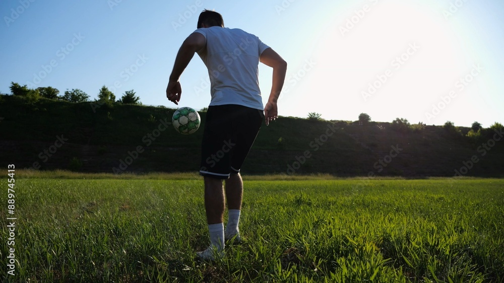 Sportsman juggling soccer ball on stadium at sunny day. Young man kicking ball at green field. Professional footballer practicing tricks at meadow with sunlight at background. Freestyle football. Sportsman juggling soccer ball on stadium at sunny day. Young man kicking ball at green field. Professional footballer practicing tricks at meadow with sunlight at background. Freestyle football.