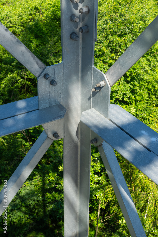 Bolted connections of steel elements of the observation tower. Construction details of galvanized steel against a green trees background