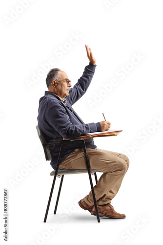 Mature man sitting in a school chair and raising hand