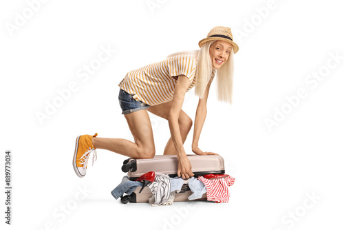 Cheerful young woman trying to close a suitcase with many clothes photo