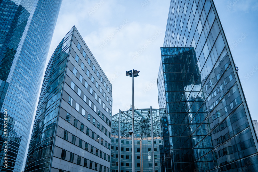 Fototapeta premium Abstract modern business architecture fragment, walls made of glass and steel with reflections of blue cloudy sky