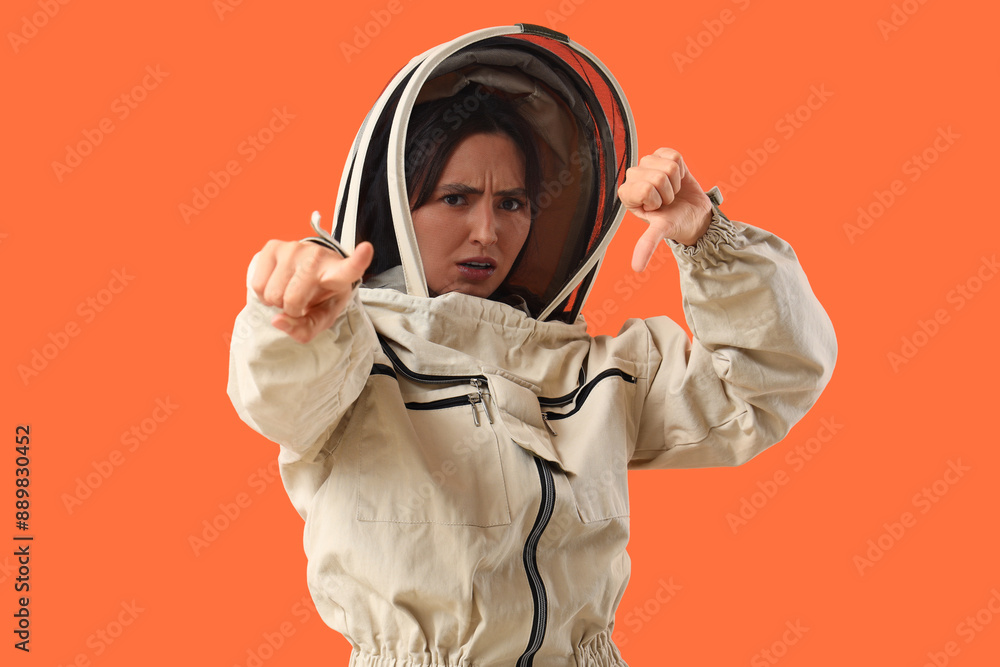 Obraz premium Female beekeeper with dislike pointing at viewer on orange background