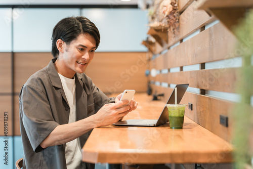 カフェでスマホとパソコンを使う若いアジア人男性 