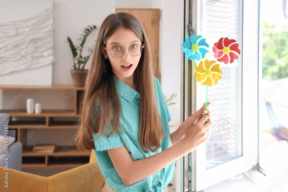 Surprised teenage girl with toy windmill near open window at home Surprised teenage girl with toy windmill near open window at home
