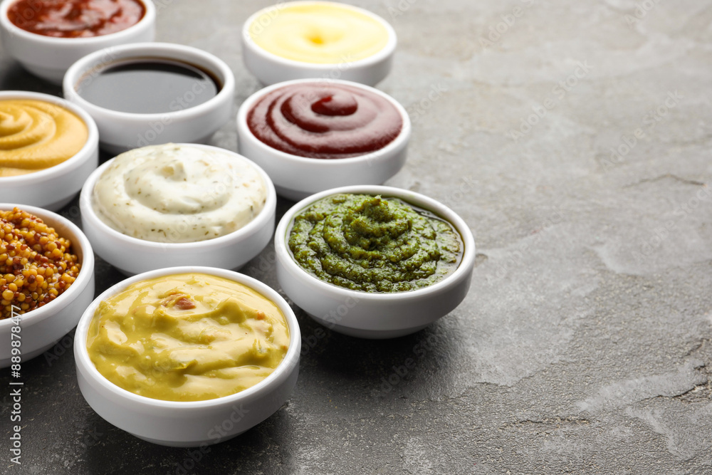 Many different sauces in bowls on grey table, closeup. Space for text Many different sauces in bowls on grey table, closeup. Space for text