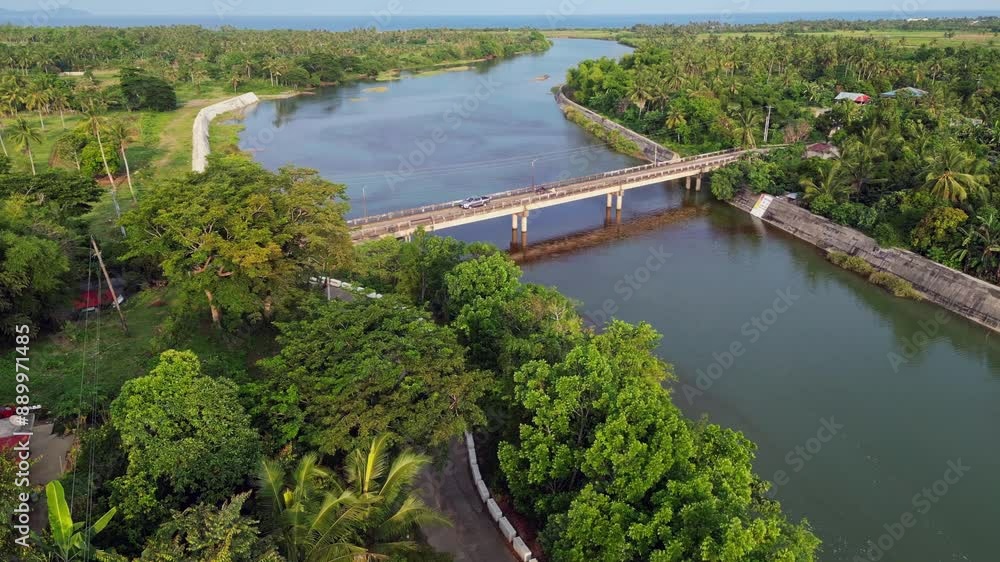 Panoramic aerial dolly of a developed provincial town with lush greenery, wide river and travelers driving across bridge in Catanduanes, Philippines Panoramic aerial dolly of a developed provincial town with lush greenery, wide river and travelers driving across bridge in Catanduanes, Philippines