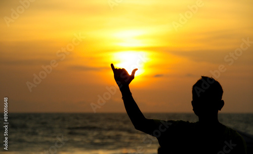 A surfer holds up a cowabunga sign in front of a beach sunset on Kuta beach in Bali Indonesia