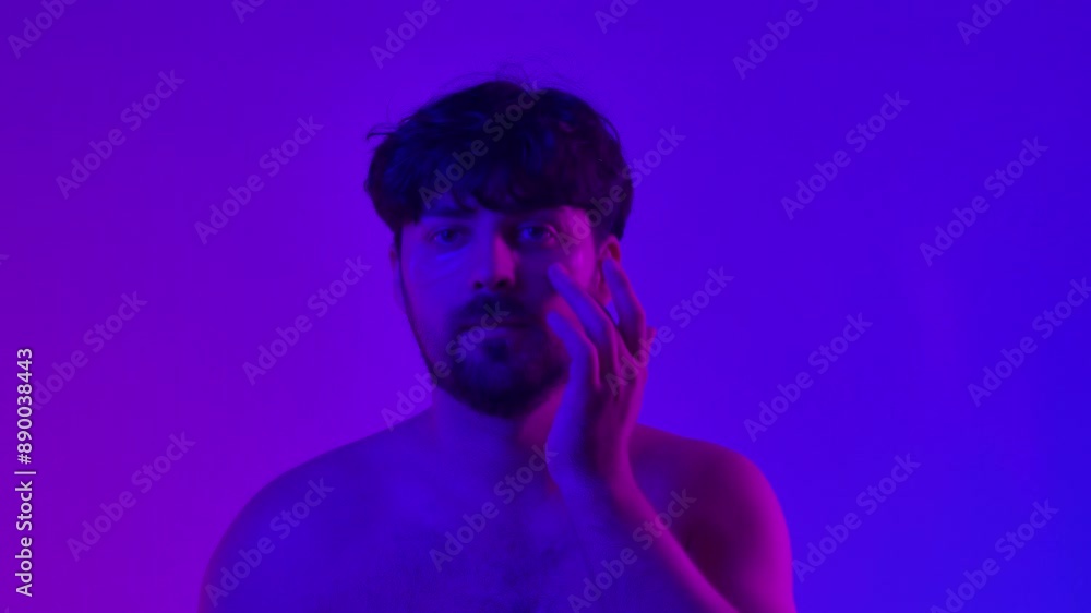 Young adult man applying eyepatch under eyes looking at camera, isolated on blue neon light background. Natural beauty skin care concept. Young adult man applying eyepatch under eyes looking at camera, isolated on blue neon light background. Natural beauty skin care concept.