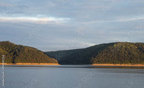 Low mountains with forests by the Dniester River. The even coastline is yellow due to the sunset 