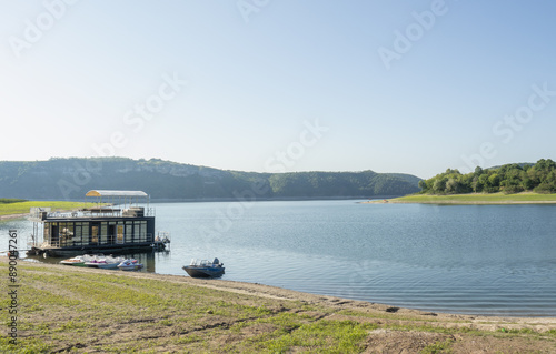 A shore of a Dniester river with a little building and powerboats on the water. There is a morning with a clear sky