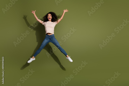 Full size photo of overjoyed girl dressed beige t-shirt jeans jumping raising palms up on black friday isolated on khaki color background © deagreez