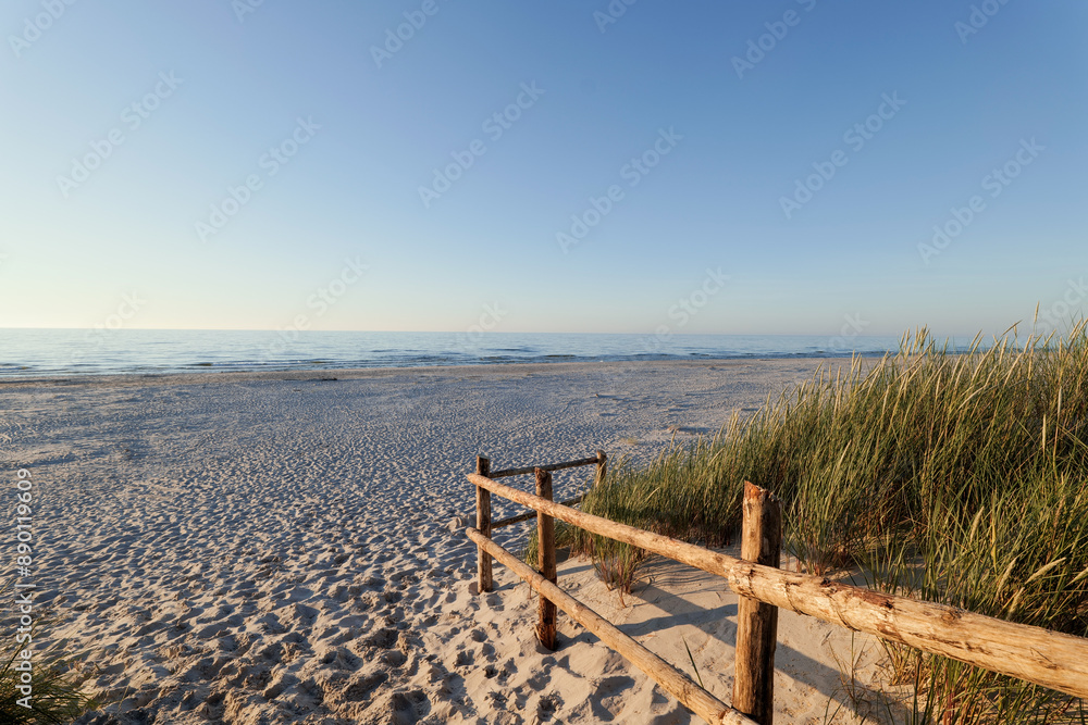 Beautiful wide beach on the Baltic Sea in the setting sun. Entrance to the beach. Wooden balustrade. Dunes covered with grass. Slajszewo, Poland