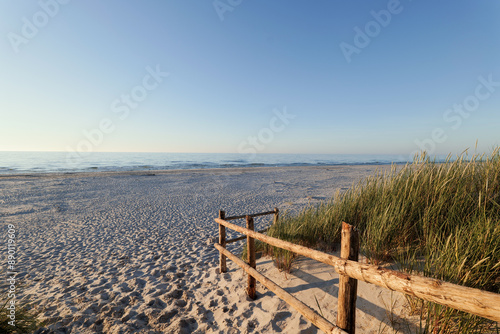 Obraz na płótnie Beautiful wide beach on the Baltic Sea in the setting sun. Entrance to the beach. Wooden balustrade. Dunes covered with grass. Slajszewo, Poland w salonie