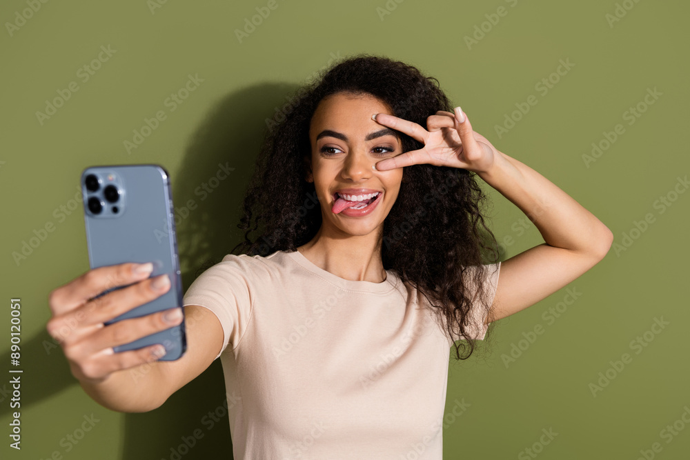 Photo of adorable girl with wavy hair dressed beige t-shirt make selfie smartphone show v-sign on eye isolated on khaki color background Photo of adorable girl with wavy hair dressed beige t-shirt make selfie smartphone show v-sign on eye isolated on khaki color background