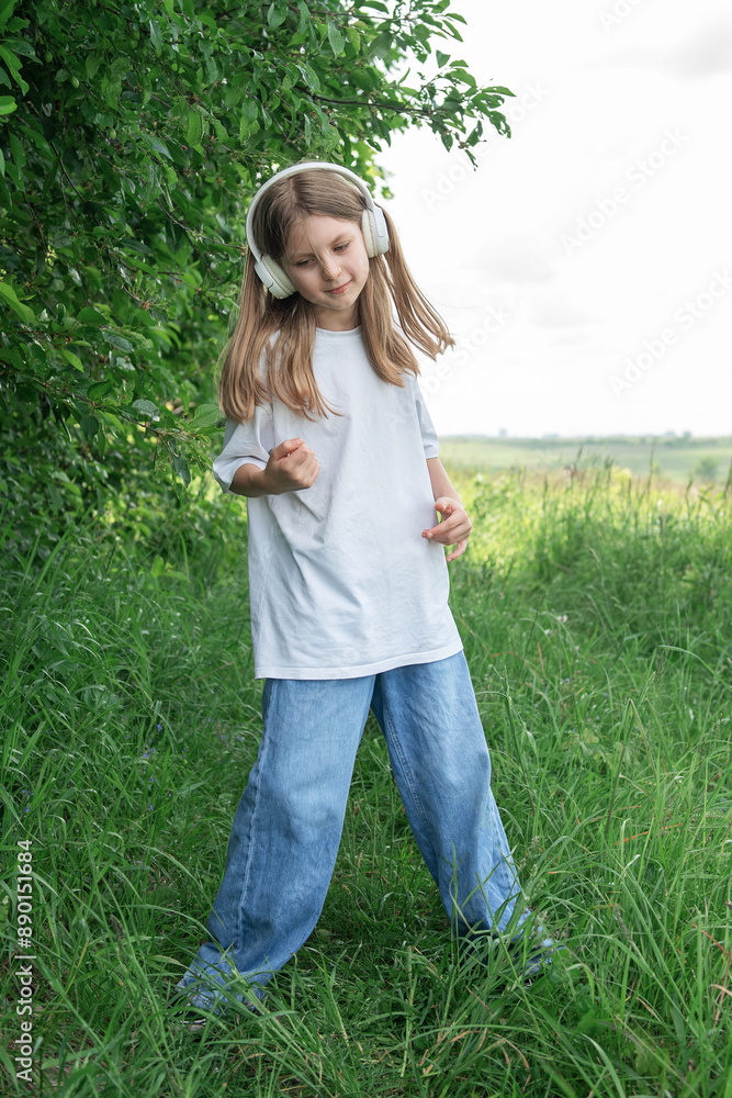 Fototapeta premium A child with headphones listening to music and dancing in the park.