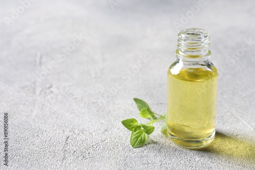 Essential oil in bottle and oregano leaves on light grey textured table, closeup. Space for text