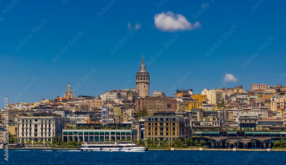 Fototapeta premium A ferry sails in the Bosphorus Strait with the Galata Tower and the Istanbul skyline in the background. A clear blue sky with a few white clouds on a sunny day.