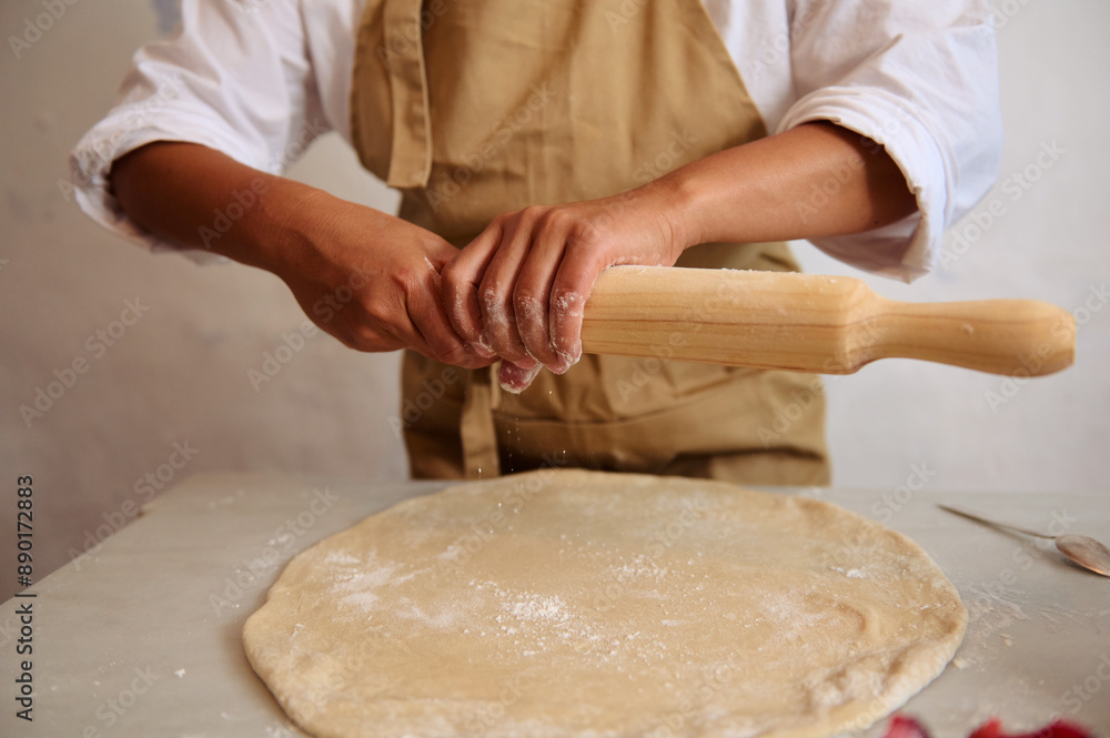 Person rolling out dough with rolling pin in kitchen. Homemade pastry preparation, artisan baking, culinary process Person rolling out dough with rolling pin in kitchen. Homemade pastry preparation, artisan baking, culinary process