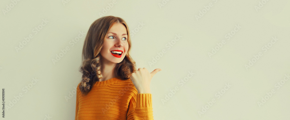 Portrait of happy smiling young woman pointing her finger to the side and looking away on white wall Portrait of happy smiling young woman pointing her finger to the side and looking away on white wall