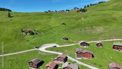 Aerial view of log cabins on green slope and reveal of mountain peaks photo