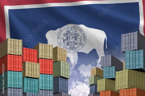 Wyoming US state flag and big stack of shipping cargo containers in docks with sky background close up photo