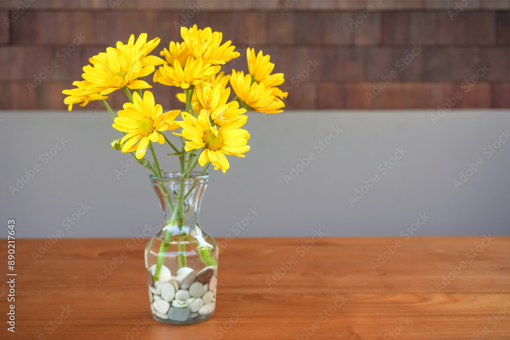Real a bunch of yellow daisy flower bouquet in transparent glass vase on wooden table. Modern interior design of modern office work room or workplace with plant. Real a bunch of yellow daisy flower bouquet in transparent glass vase on wooden table. Modern interior design of modern office work room or workplace with plant.