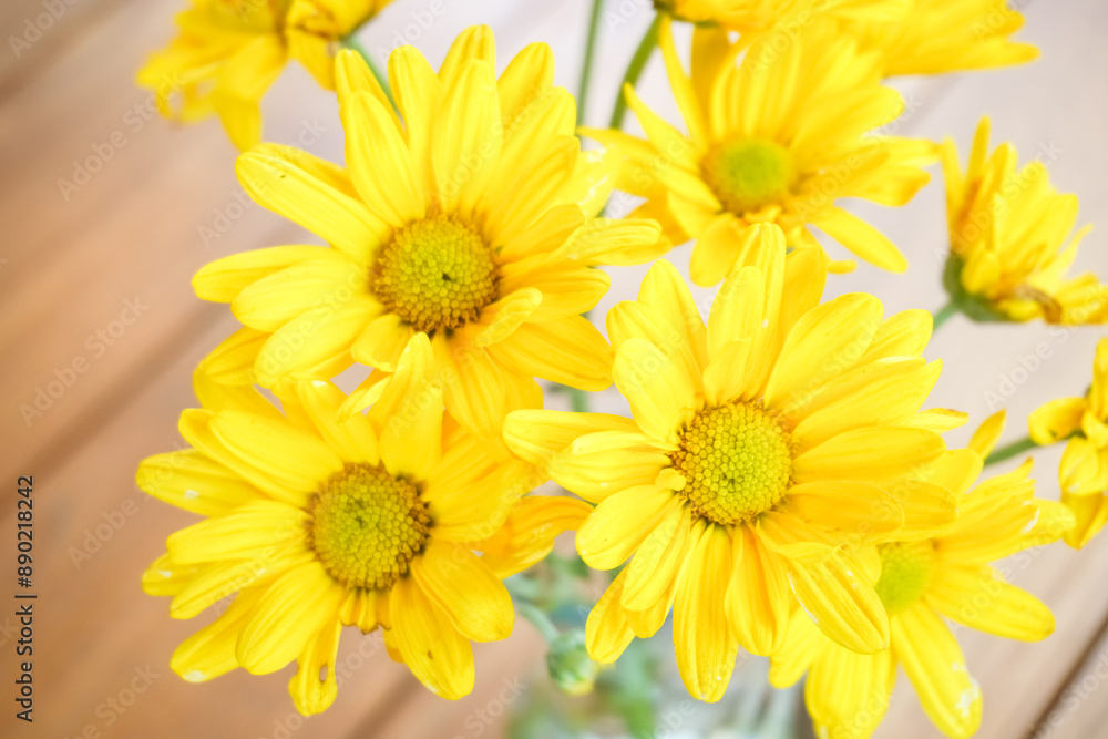 Close up photo of a bunch of yellow daisy flower bouquet in transparent glass vase on wooden table. Modern interior design of modern office work room or workplace with plant. Close up photo of a bunch of yellow daisy flower bouquet in transparent glass vase on wooden table. Modern interior design of modern office work room or workplace with plant.
