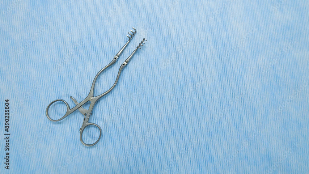 Fototapeta premium A Weitlaner self-retractor used in heart surgery placed on a blue background. Medical instruments used in the operating room. Surgical clamp with retainer.