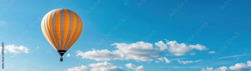 Obraz premium A colorful hot air balloon floating in a clear blue sky with scattered clouds, exemplifying adventure and freedom in a serene landscape.