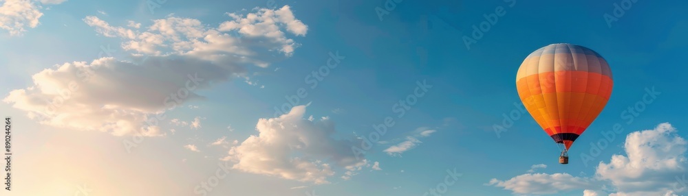 Obraz premium A vibrant hot air balloon floating in a clear sky with scattered clouds, creating a serene and inspiring scene perfect for travel or adventure concepts.
