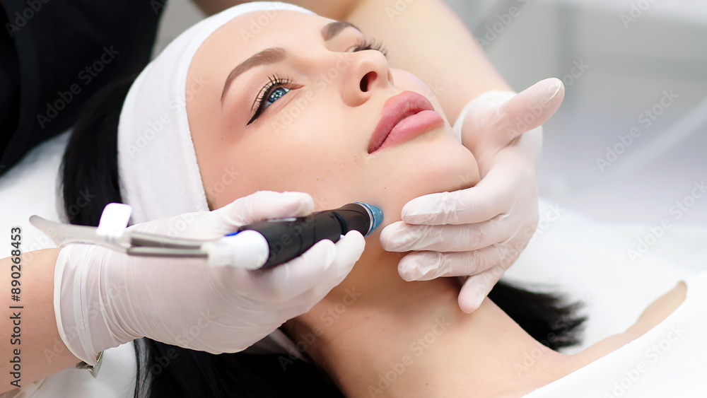 A cosmetologist does a hydrofacial procedure on a woman's face in a modern beauty clinic. Concept of cosmetology, care and healthy skin. A cosmetologist does a hydrofacial procedure on a woman's face in a modern beauty clinic. Concept of cosmetology, care and healthy skin.