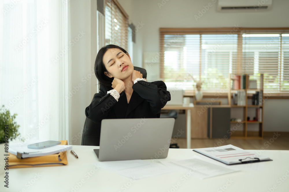 Tired young businesswoman massaging her neck and shoulders, indicating fatigue or muscle tension Tired young businesswoman massaging her neck and shoulders, indicating fatigue or muscle tension