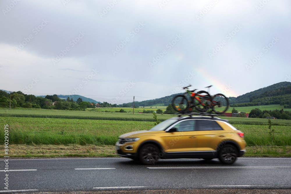 Fototapeta premium Samochód osobowy, SUV z rowerami na dachu w tle tęcza nad górami.