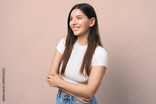 Radiant young woman in a white shirt, smiling with arms crossed and hair tucked behind her ear, exuding confidence and joy. Ideal for lifestyle, confidence, and modern fashion themes