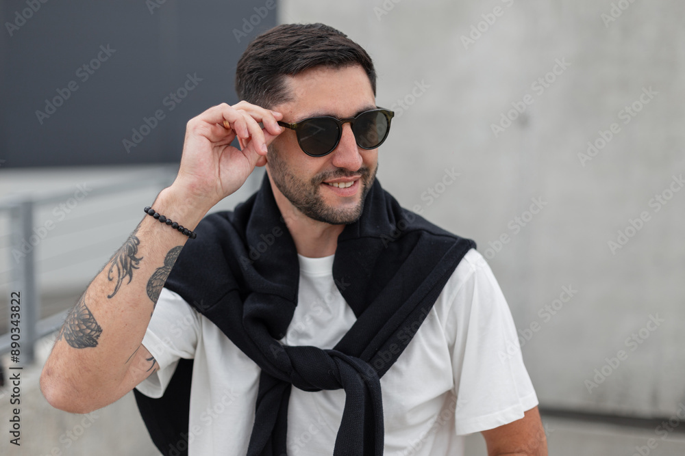 cool happy fashionable successful business man with a hairstyle in casual clothes with a sweater walks in the city on a concrete background and puts on fashion sunglasses eyewear cool happy fashionable successful business man with a hairstyle in casual clothes with a sweater walks in the city on a concrete background and puts on fashion sunglasses eyewear
