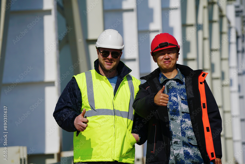Two multiracial construction workers or engineers walking side by side through a construction site, conversing. Two multiracial construction workers or engineers walking side by side through a construction site, conversing.